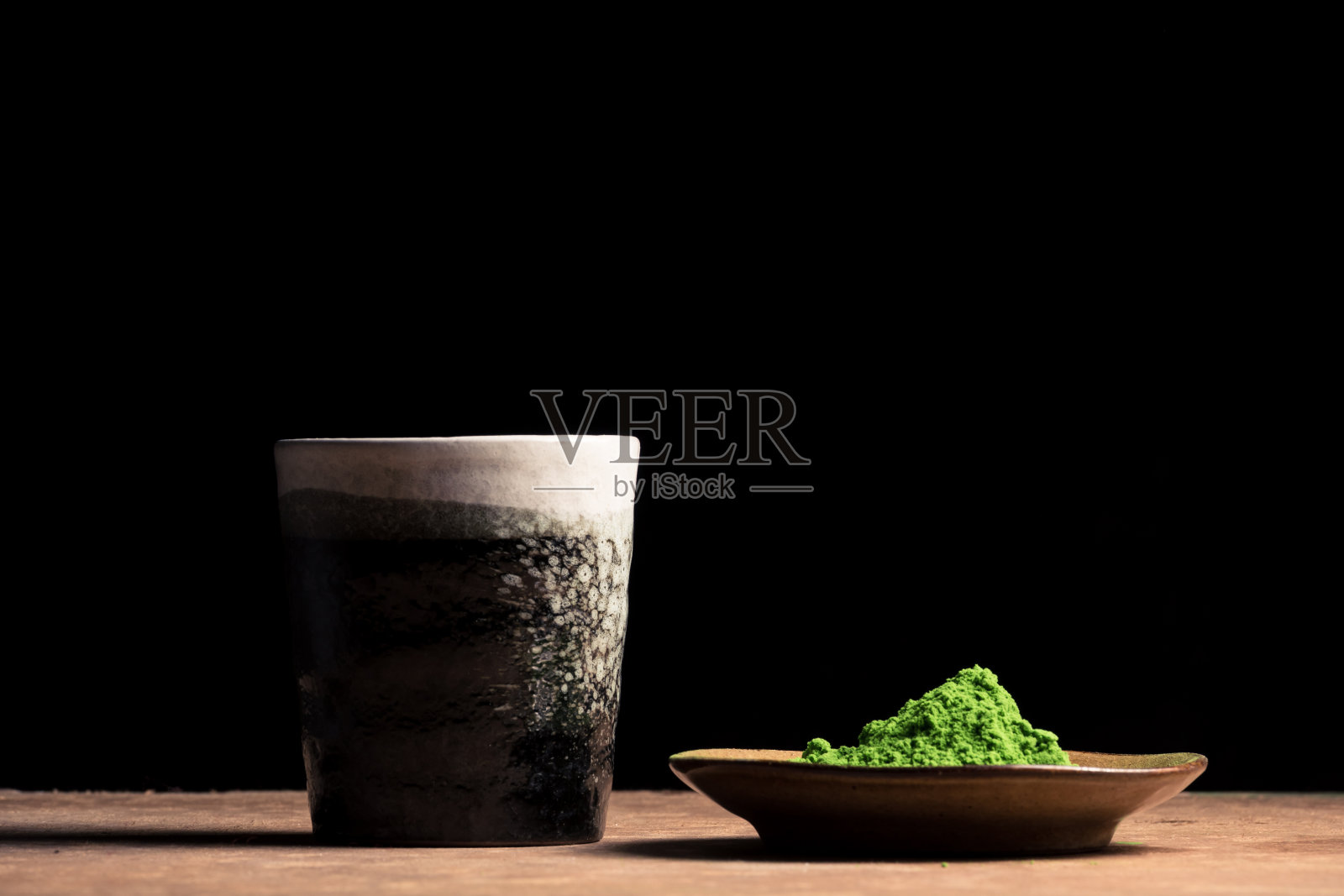 桌上有一只瓷杯和绿茶粉，背景是黑色的。文本的空闲空间照片摄影图片