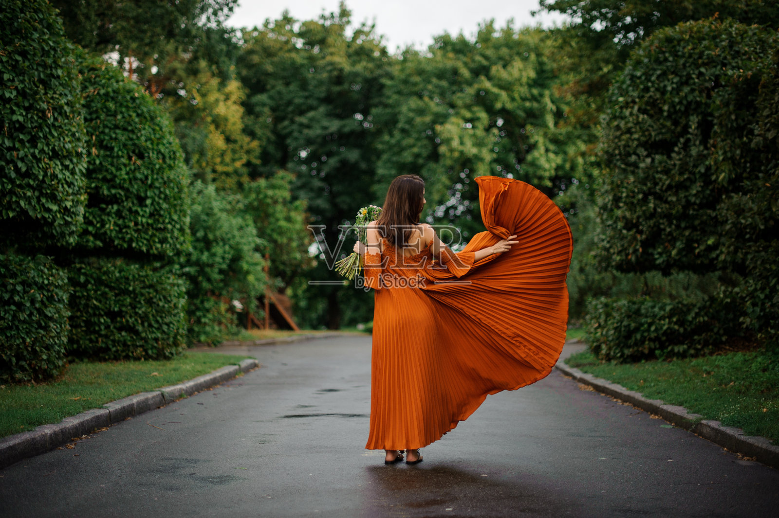 背影迷人的女人在长橙色连衣裙与鲜花照片摄影图片