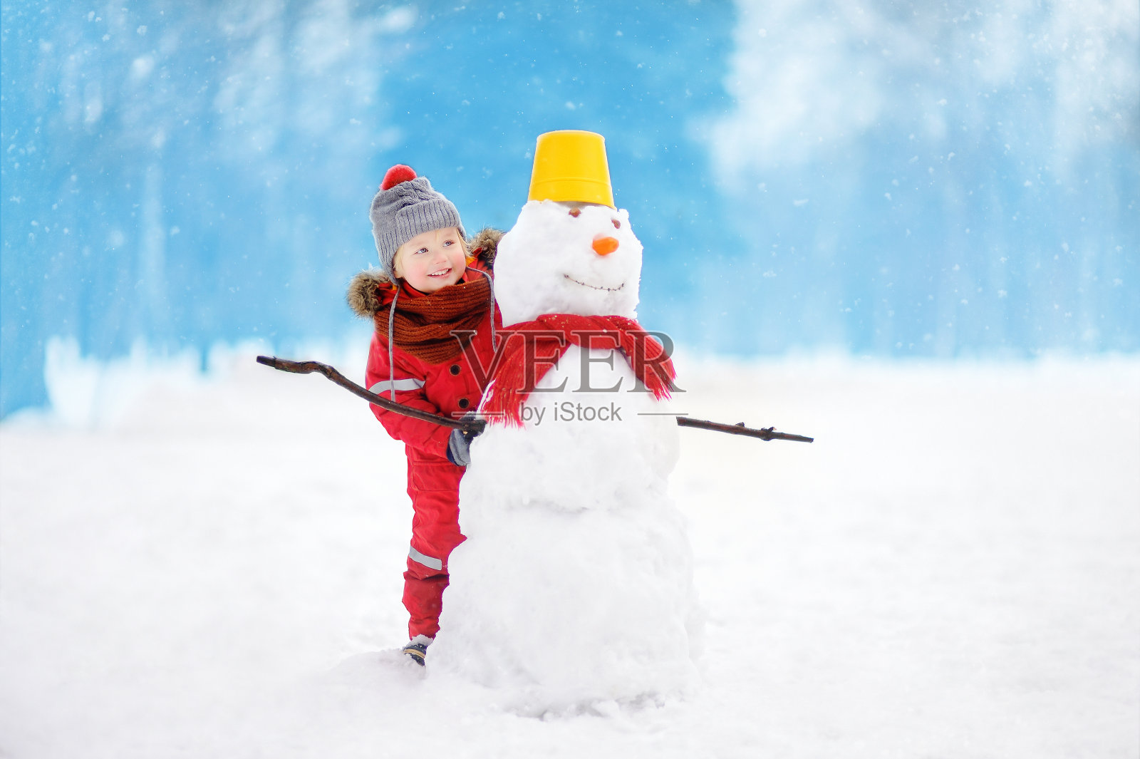 穿着红色冬衣的小男孩在雪天公园里玩雪人照片摄影图片