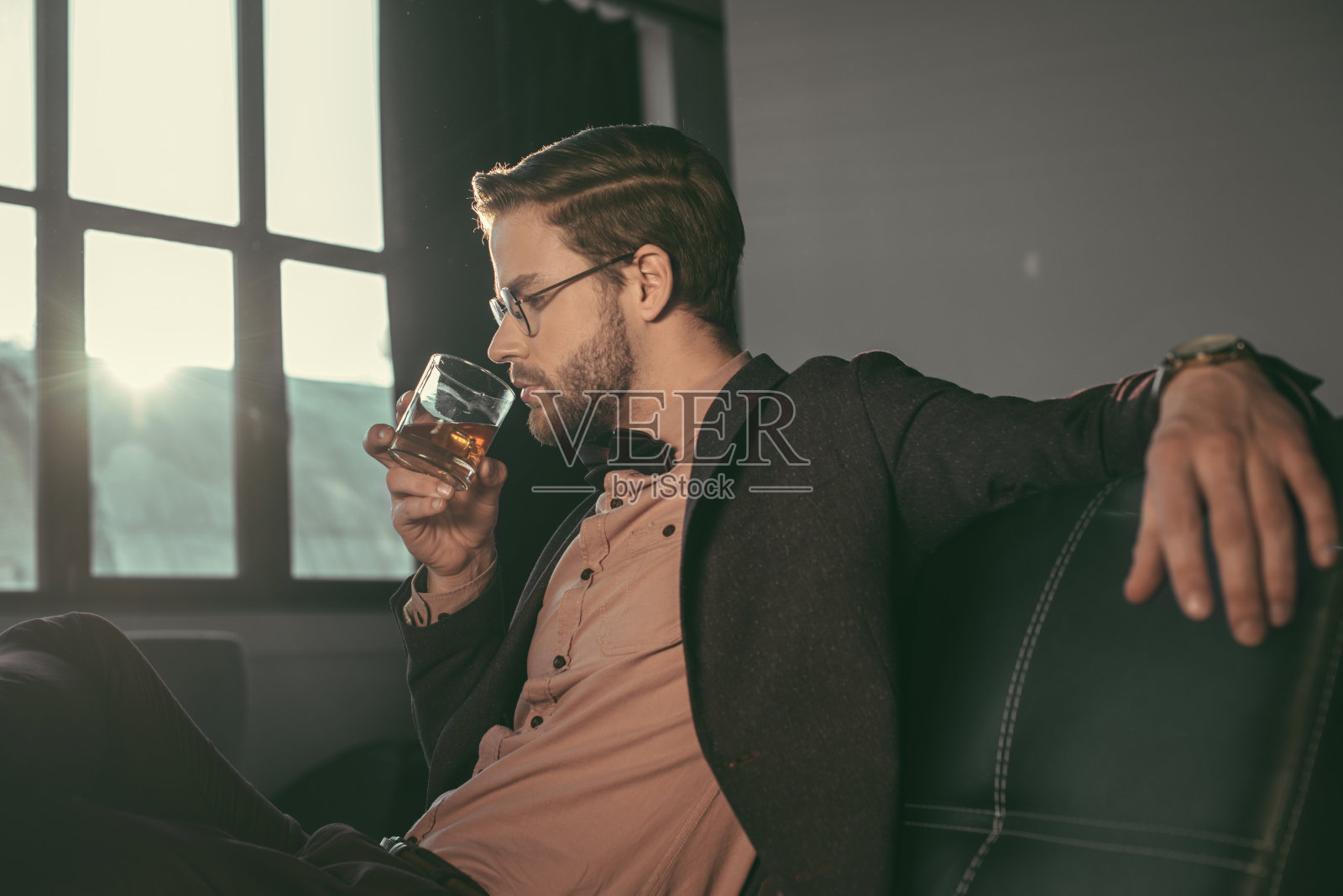 戴着眼镜，打着领结，喝着威士忌的时髦年轻商人照片摄影图片