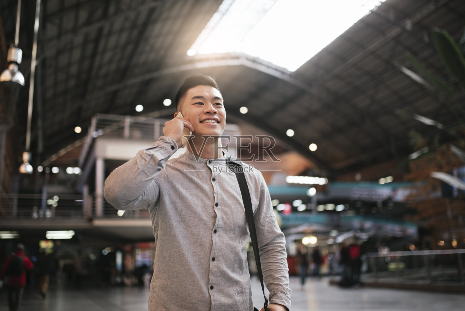 英俊的亚洲男人在火车站用手机。照片摄影图片