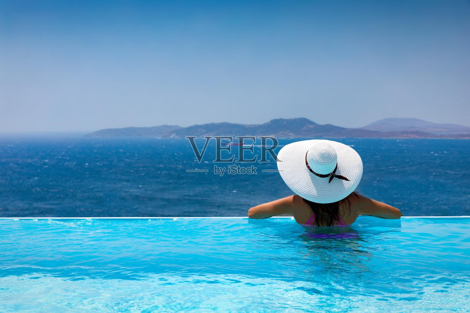 迷人的女人享受从游泳池到地中海的景色照片摄影图片