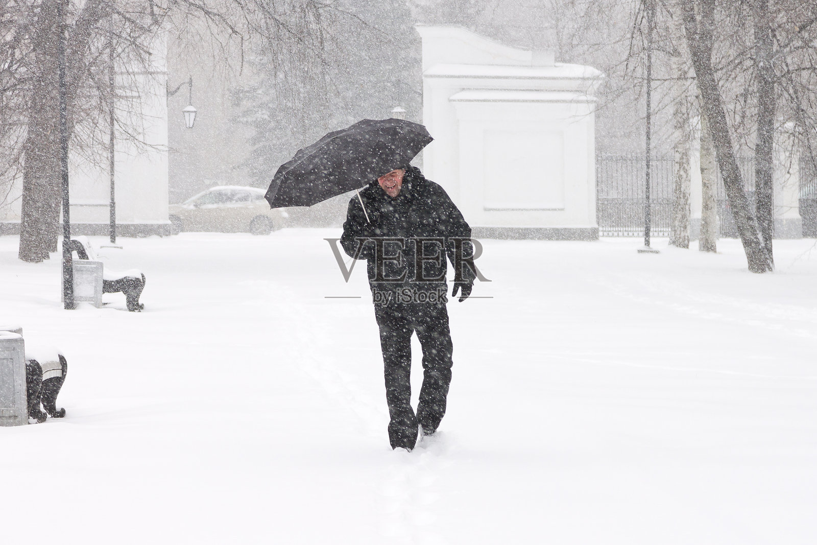 冬天城市的天气非常糟糕:可怕的大雪和暴风雪。男行人躲在伞下躲避积雪照片摄影图片