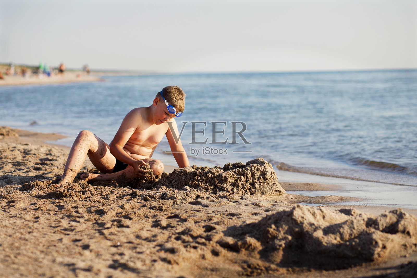 一个男孩正在海滩上建沙堡。照片摄影图片