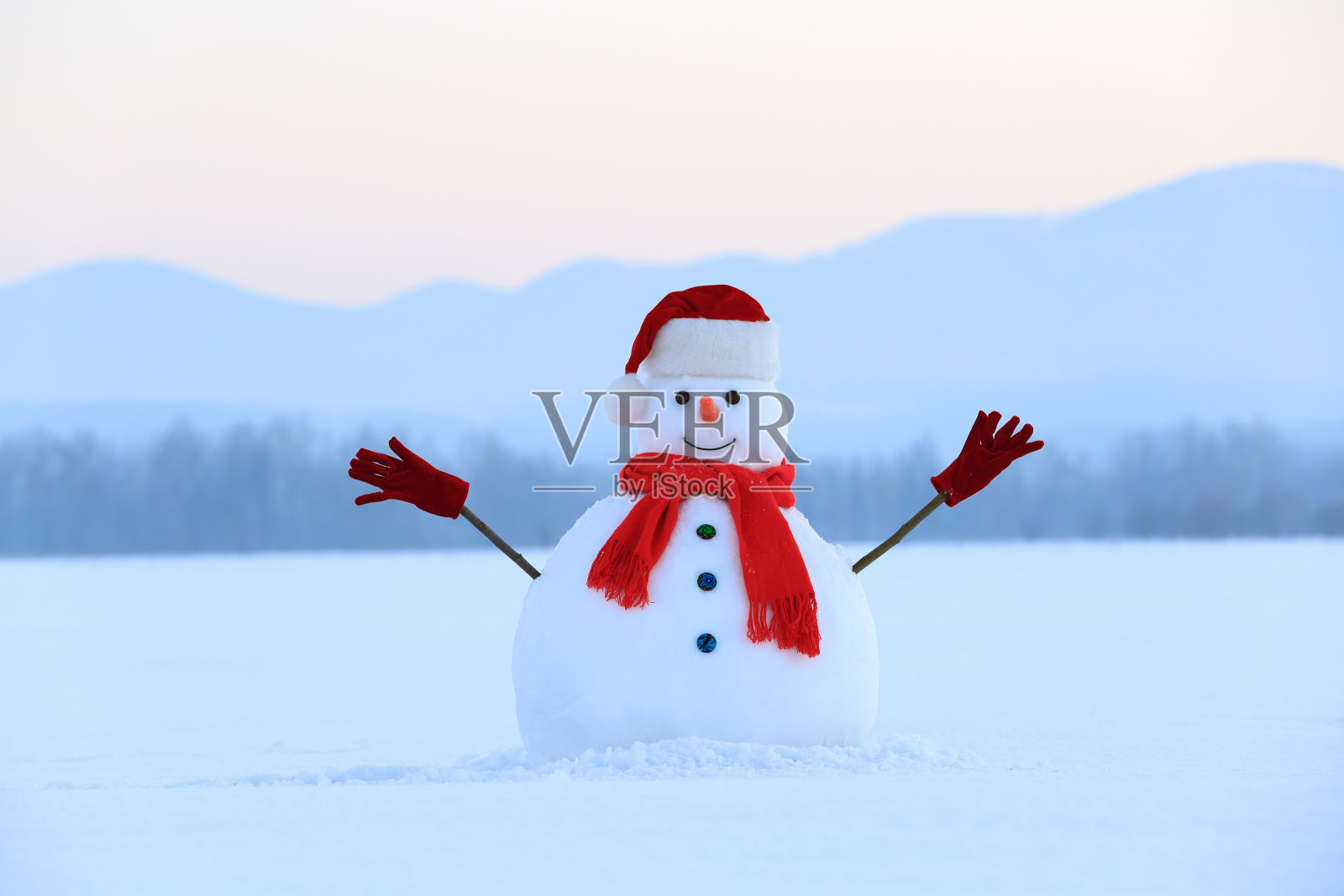 戴着红帽子和围巾的雪人。圣诞节的风景。背景是高山。地面被雪覆盖。寒冷的冬天。照片摄影图片