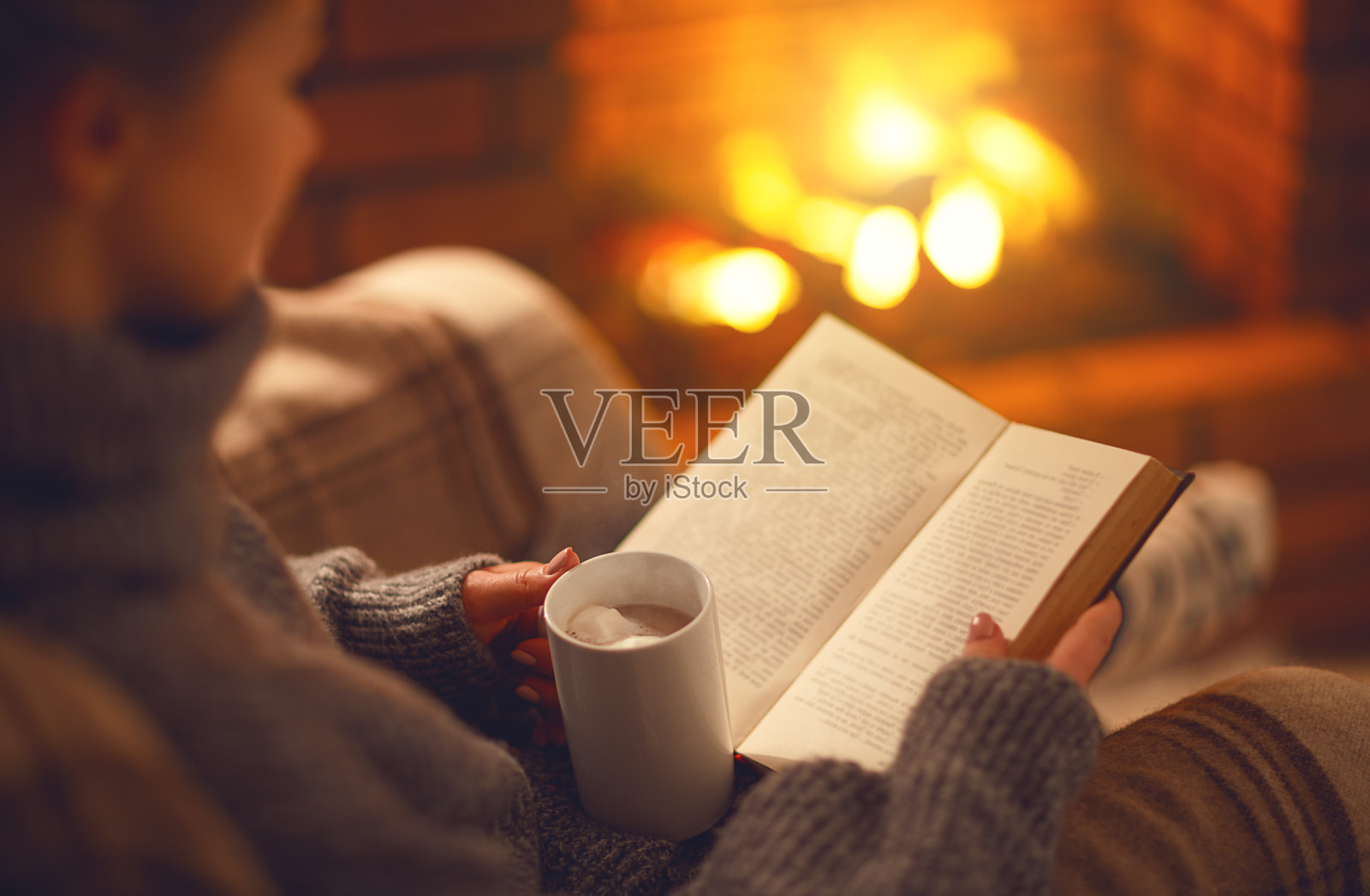 冬日傍晚，壁炉旁，女孩手里拿着一本书和一杯咖啡照片摄影图片