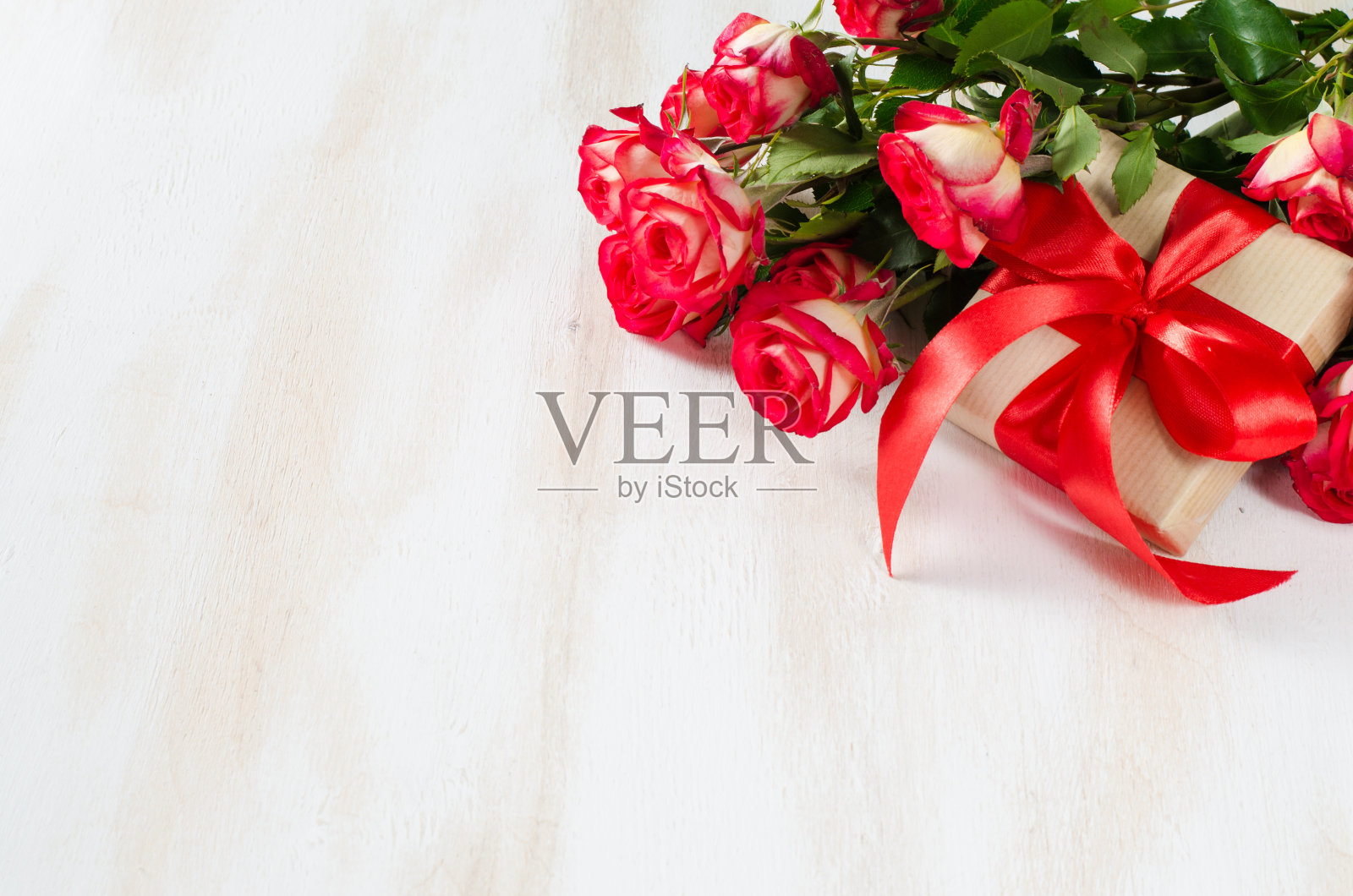 红玫瑰花束和礼物放在木桌上。照片摄影图片