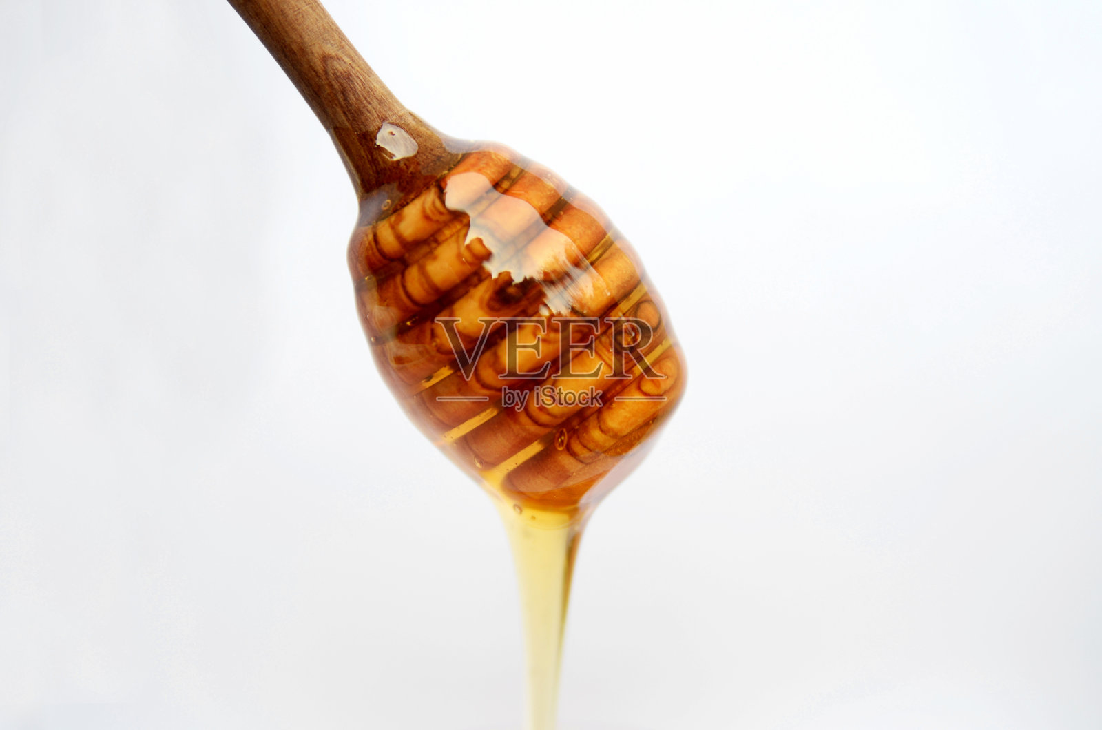 蜂蜜从木棒勺上滴下孤立灰色。健康的黄金粘性天然蜂产品。照片摄影图片
