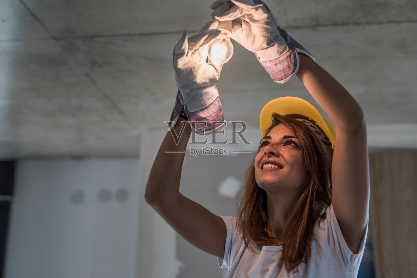 年轻快乐的手工工人在装修公寓修理灯。照片摄影图片