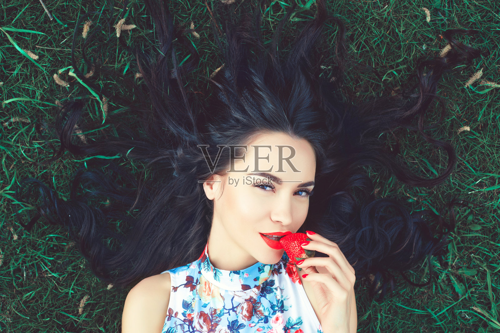 美丽的年轻女子在草地上，嘴里叼着草莓照片摄影图片