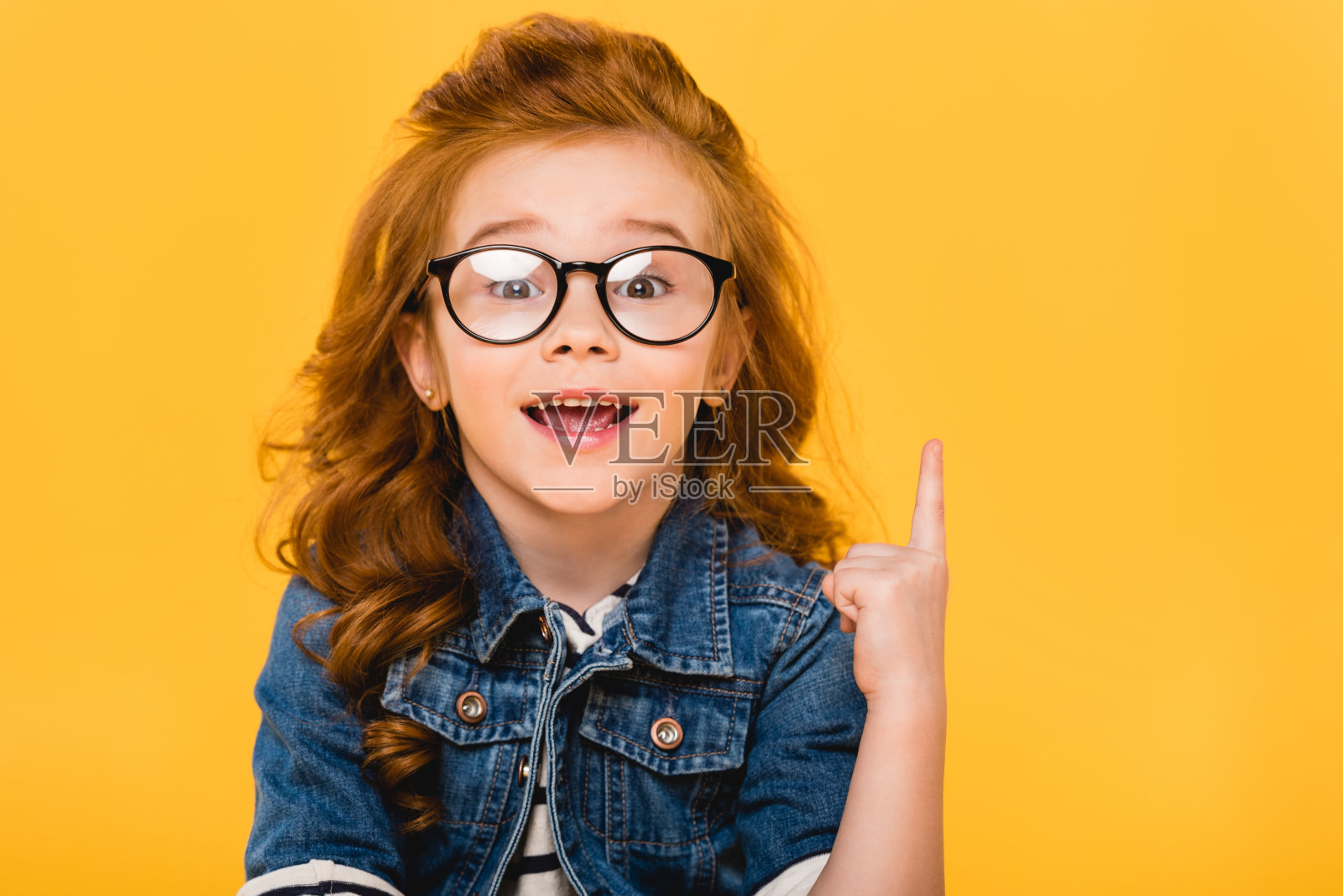 一个带着眼镜的微笑的小孩的肖像，孤立地指向黄色照片摄影图片