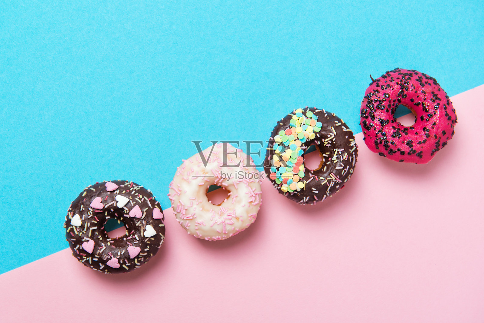 各色的甜甜圈排成一排，极简主义的蓝色和粉红色的背景，俯视图照片摄影图片