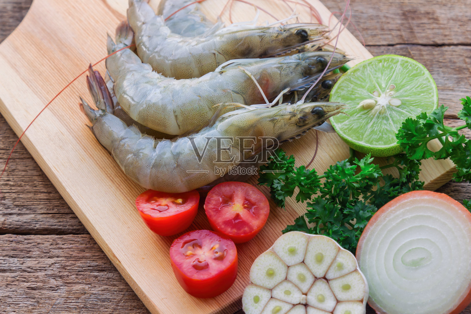 在近距离观察新鲜的白色虾木切板。在木桌上为海鲜菜单准备生虾、蔬菜和香草。自制美味食物的概念。照片摄影图片