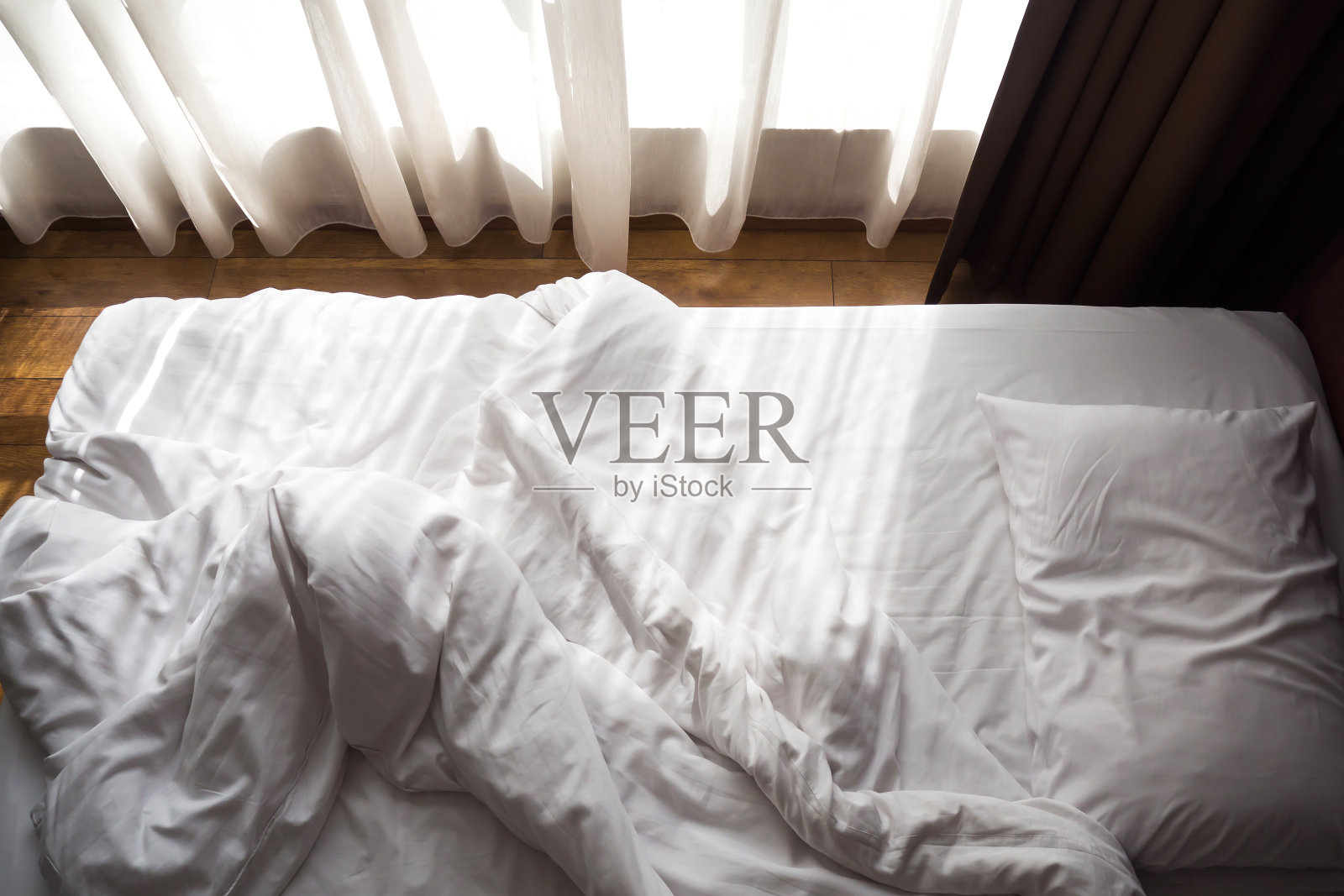 凌乱的床上。白色的枕头和毯子，阳光透过窗户。放松的概念。照片摄影图片