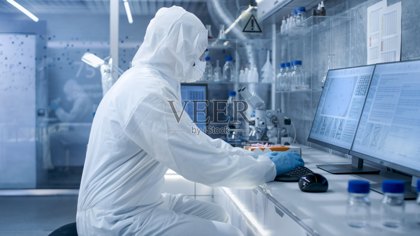 在一个安全的高水平实验室里，科学家们穿着工作服进行一项研究。生物学家在计算机上分析结果。照片摄影图片