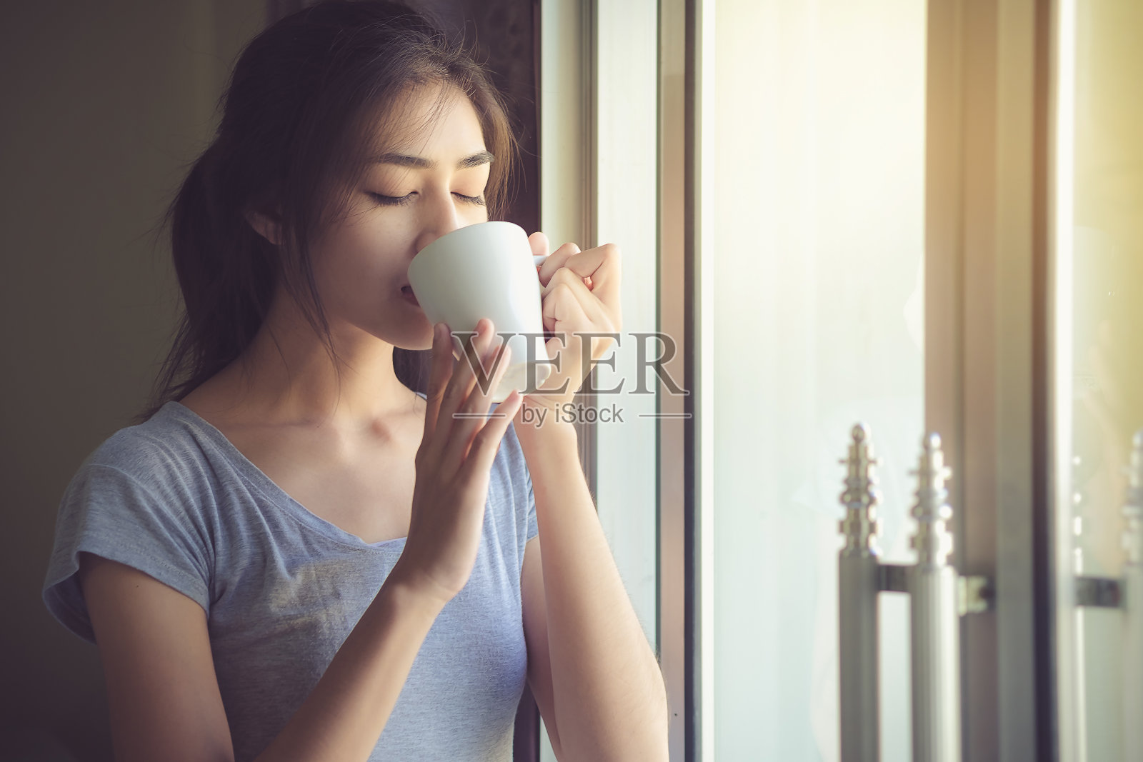 可爱的女人在周末愉快地喝着咖啡，窗外有一缕阳光。生活方式的概念照片摄影图片
