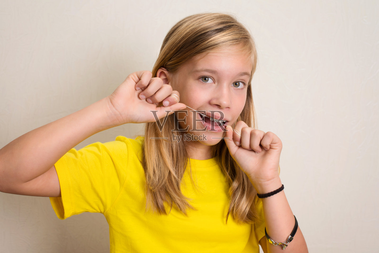 带牙套的女孩用牙线剔牙。特写肖像的少女与牙线孤立。照片摄影图片