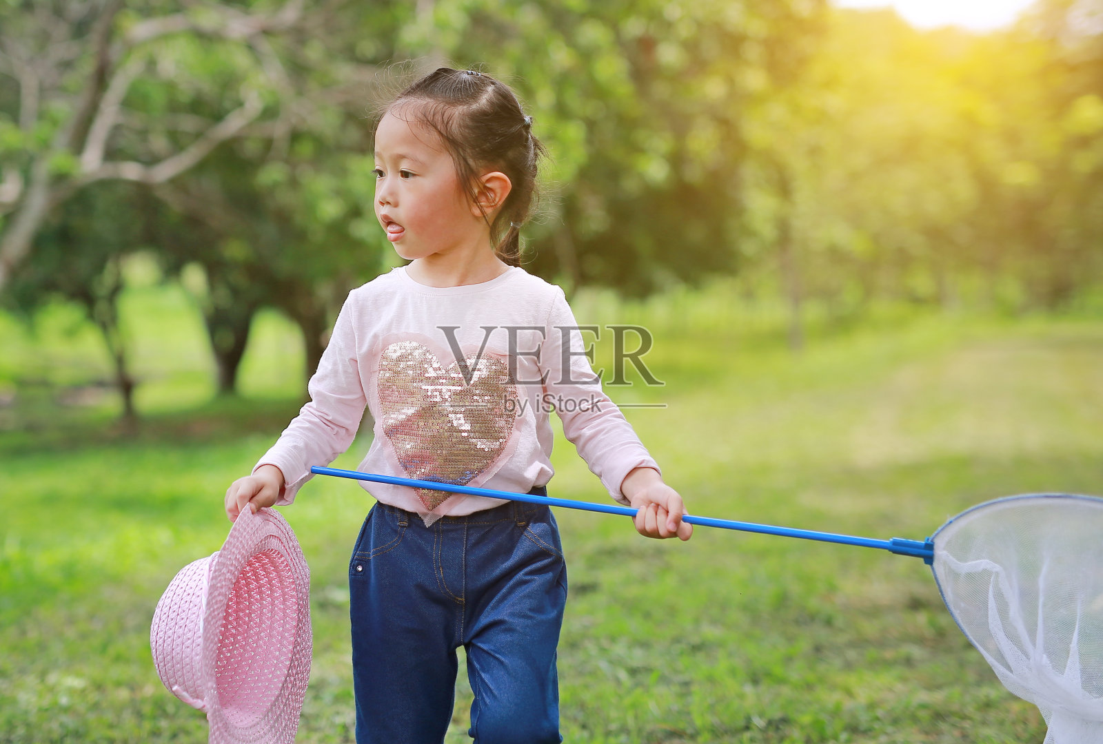 一个亚洲女孩在夏天用虫网在田野里玩。照片摄影图片