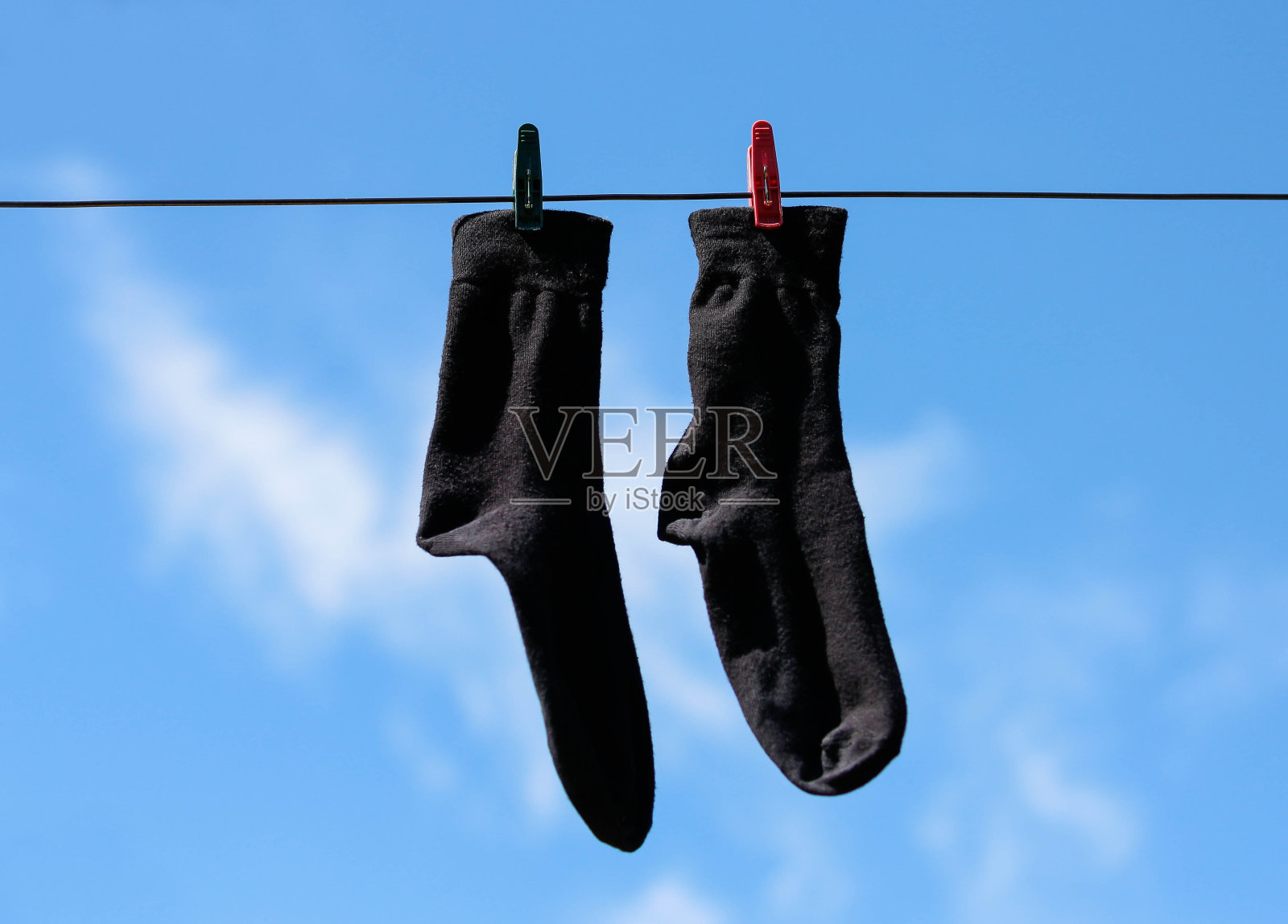 黑袜子用晒衣夹挂在晒衣绳上晾晒。特写镜头。在蓝天白云的背景上照片摄影图片