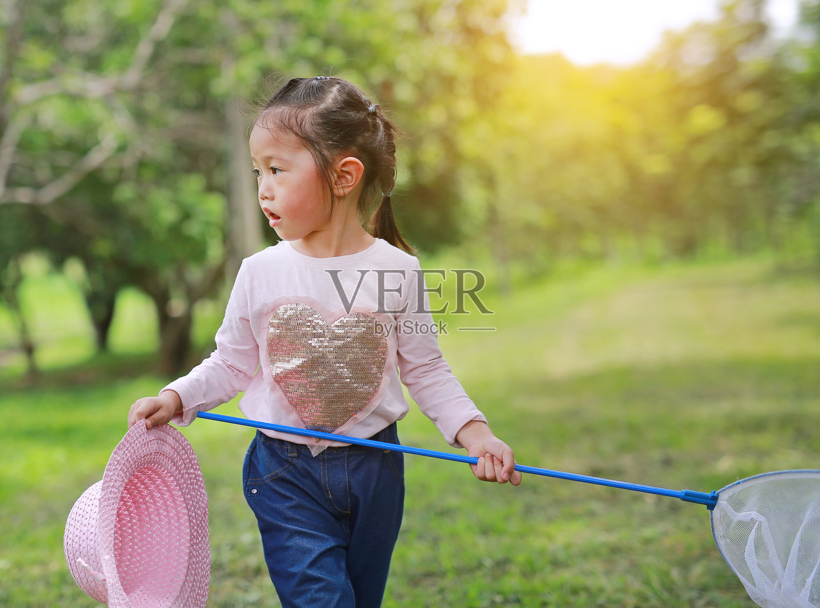 可爱的亚洲女孩戴着草帽和蚊帐在田野里玩夏天。照片摄影图片