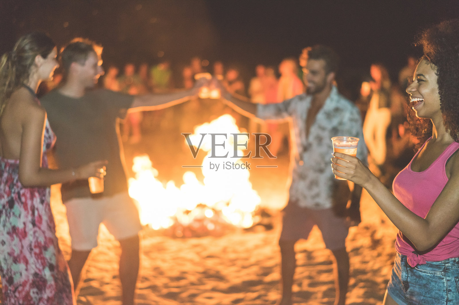 快乐的朋友喝啤酒在海滩节日与篝火的背景-年轻人有乐趣的暑假-青年，假期和派对的概念-软焦点非洲女孩手玻璃-温暖的过滤器照片摄影图片