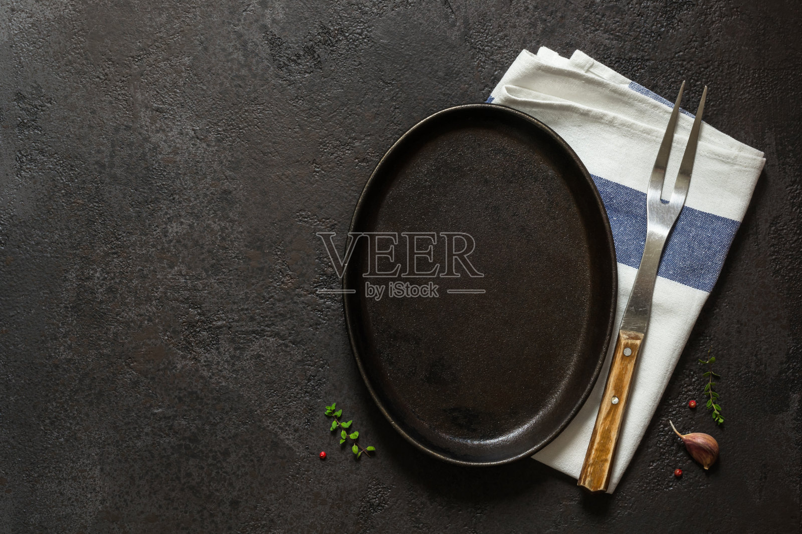 黑暗的烹饪背景。空铸铁盘，餐巾和叉子照片摄影图片
