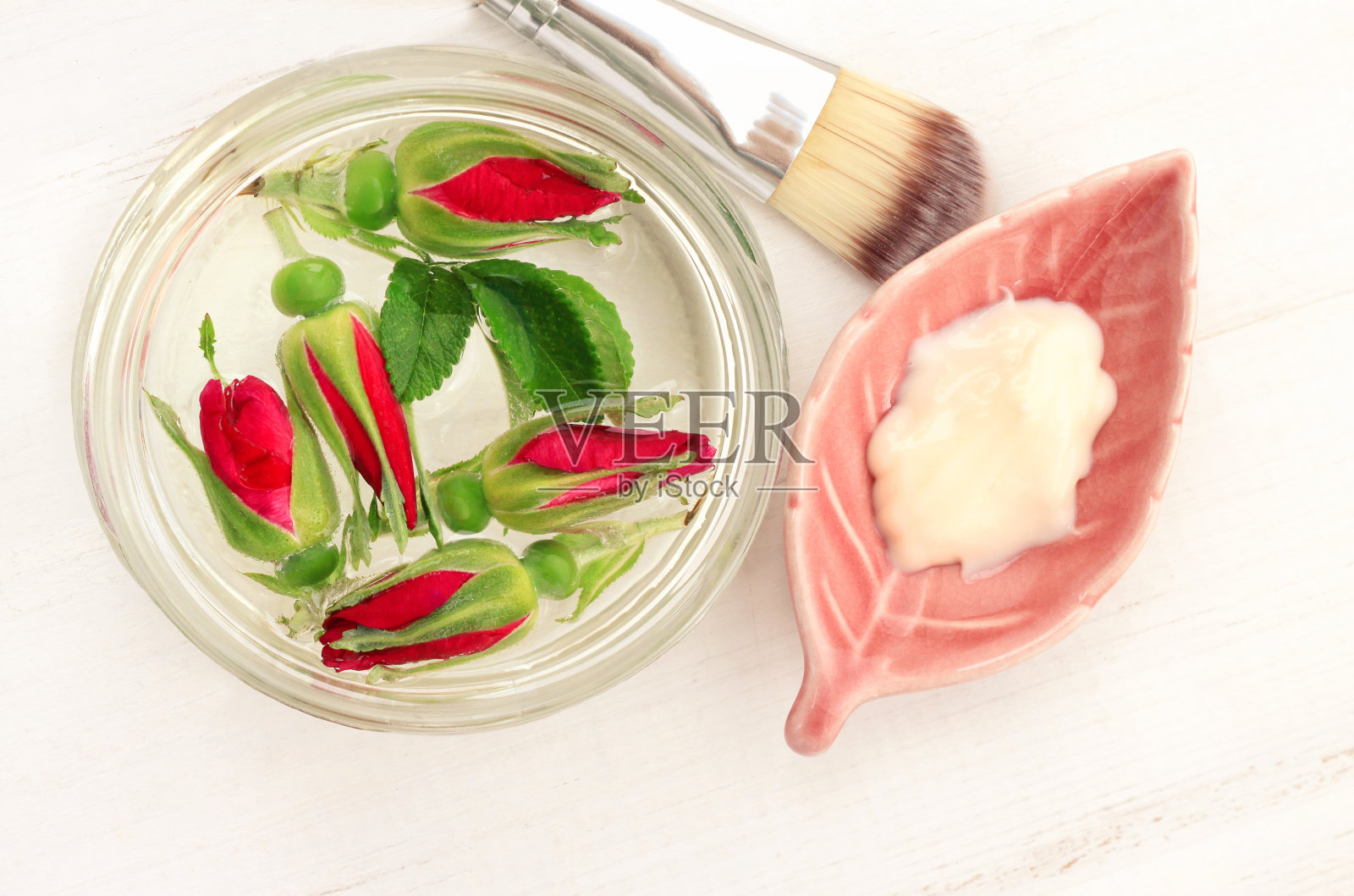 玫瑰面膜化妆产品在粉红色陶瓷板，玻璃瓶玫瑰水与花照片摄影图片
