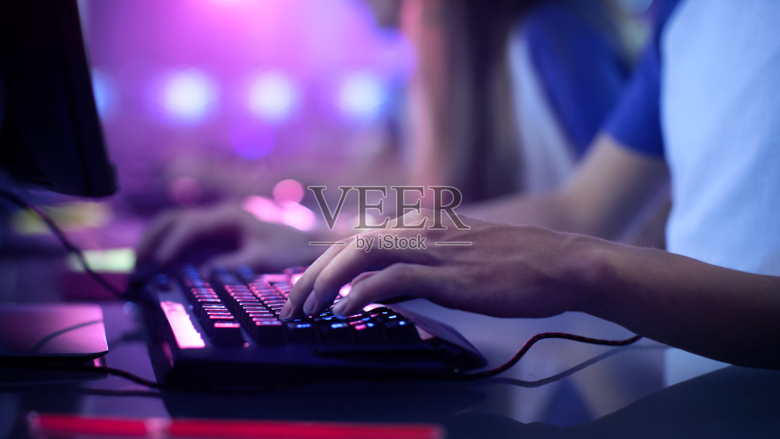 玩家手在键盘上的特写，积极按按钮，玩MMO在线游戏。背景是霓虹灯。照片摄影图片