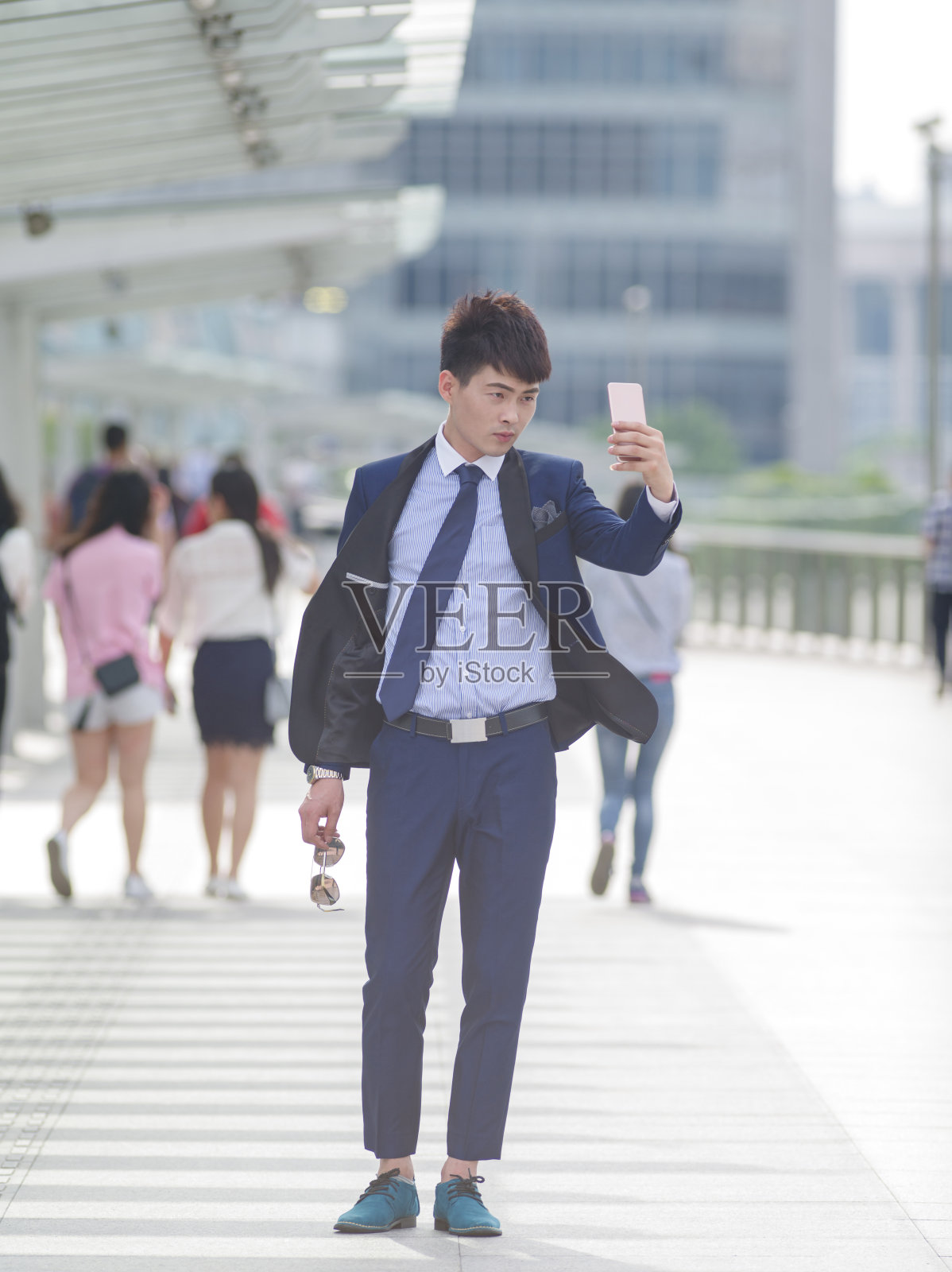 在中国上海的大街上，一名穿着西装的帅气青年正在用手机自拍。照片摄影图片