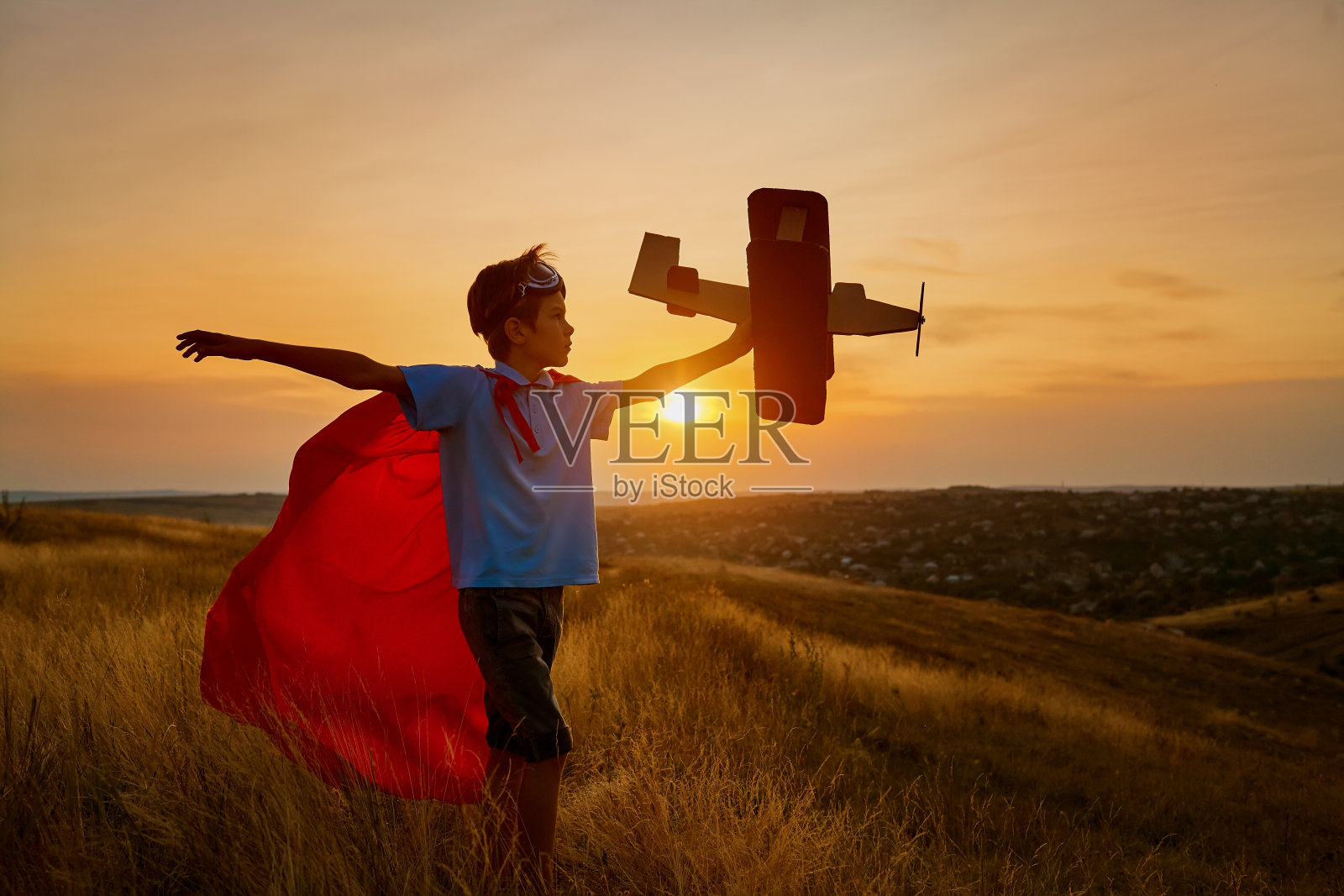 一个穿着超级英雄服装的快乐男孩正在玩一架飞机。照片摄影图片
