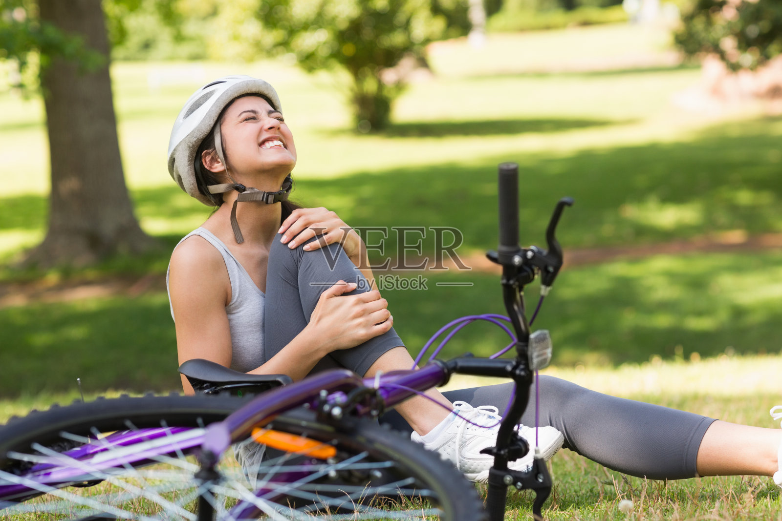 女自行车手受伤的腿坐在公园里照片摄影图片