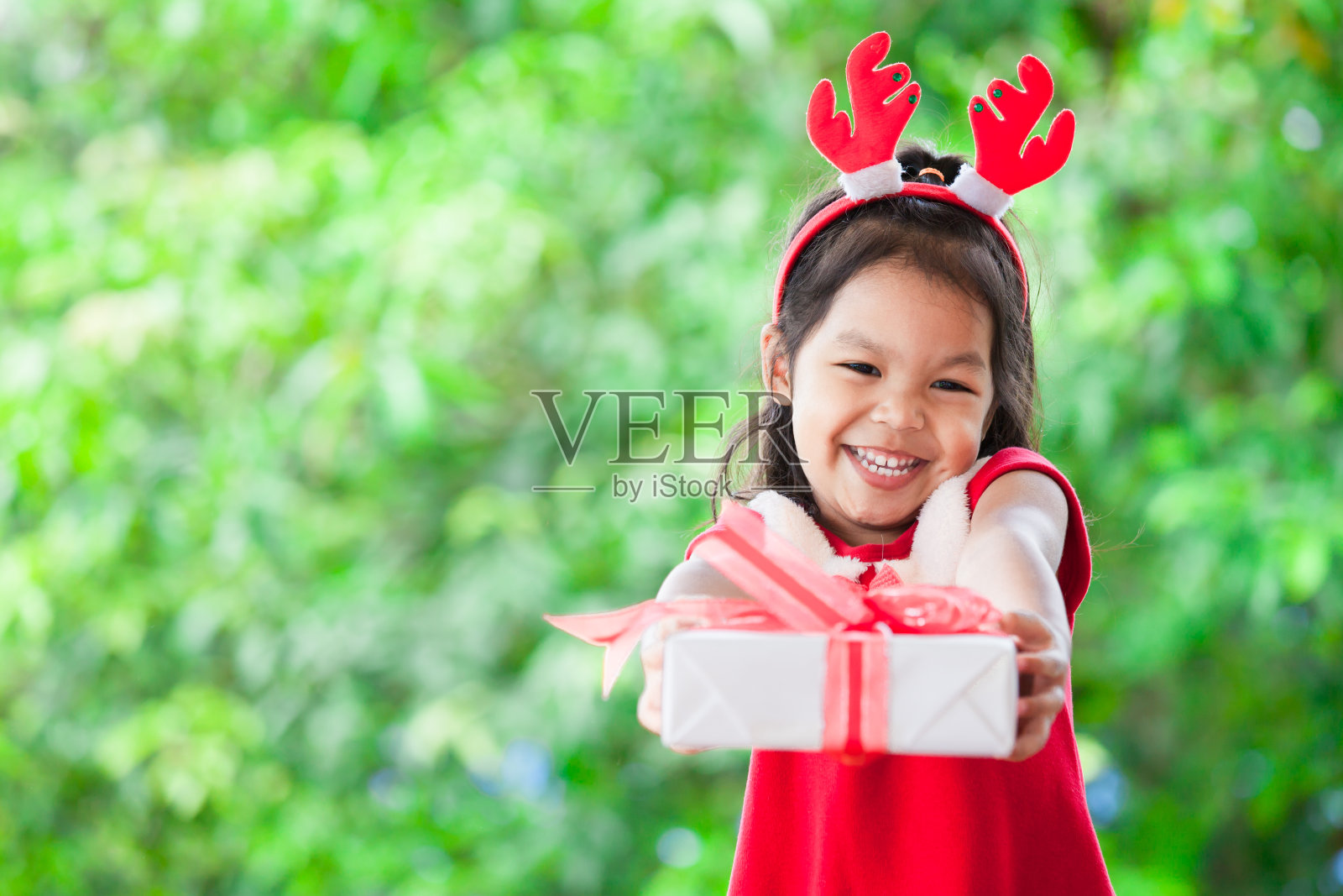 可爱的亚洲儿童女孩抱着并给予绿色自然背景的圣诞礼物照片摄影图片