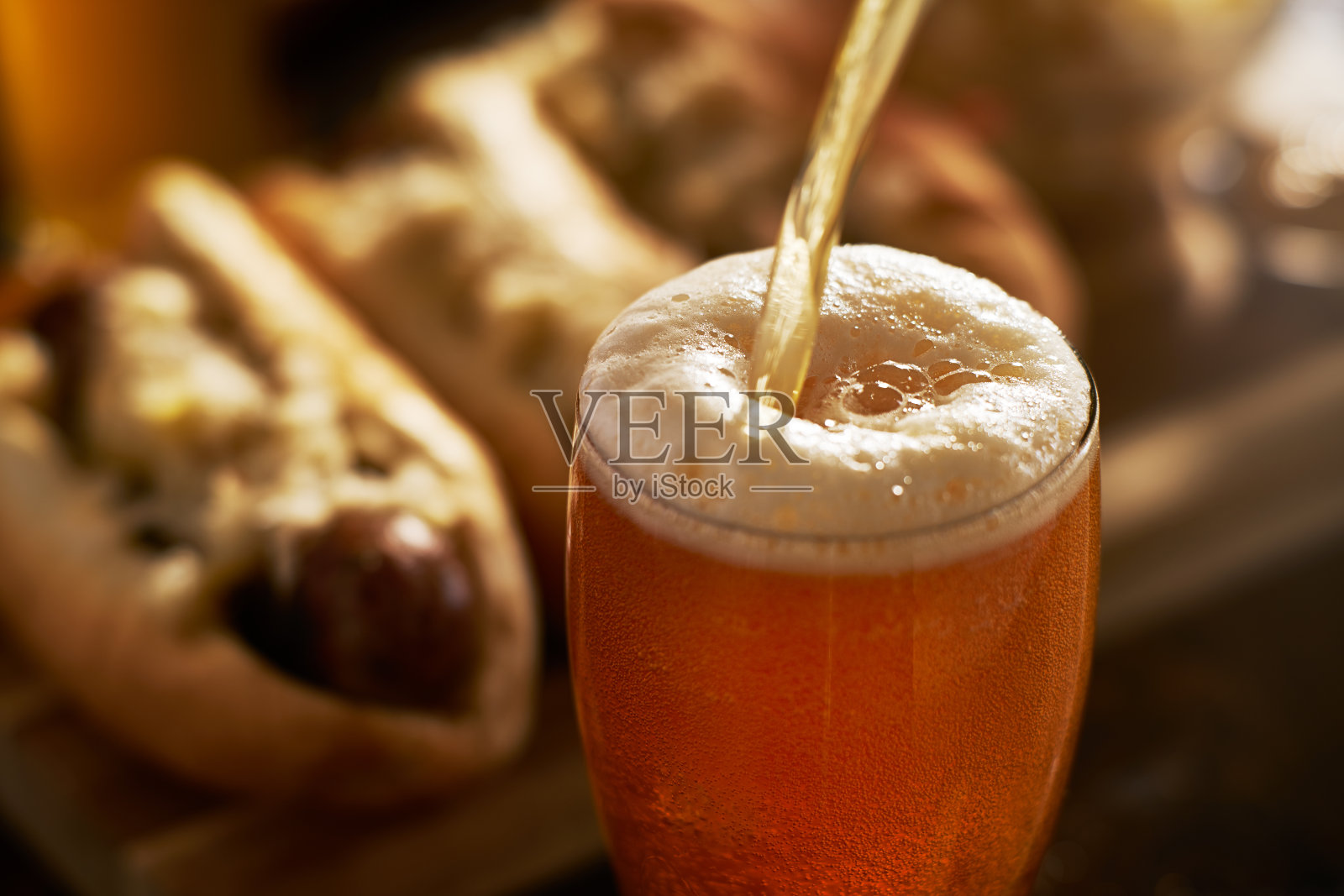 将深色印度淡啤酒倒入背景为德国香肠的马克杯中照片摄影图片
