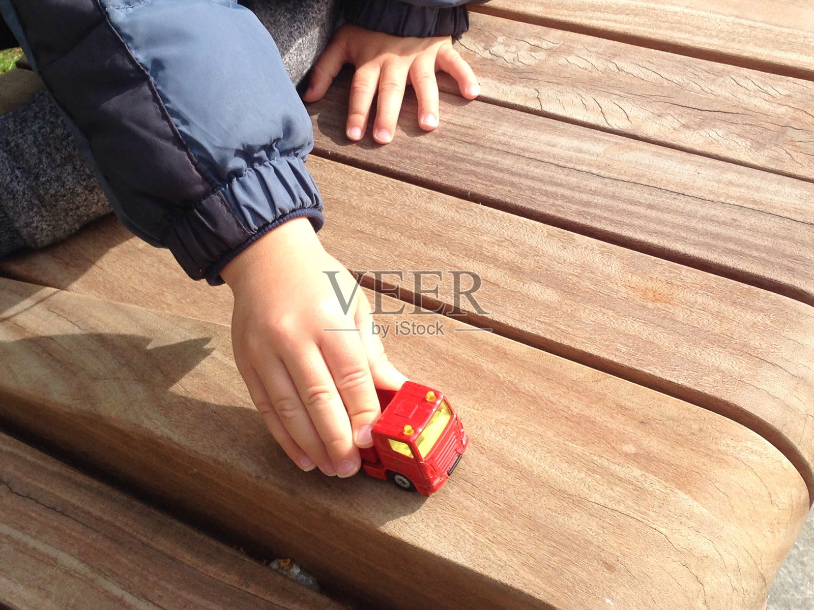 在伦敦，孩子在户外的木凳上玩红色的汽车照片摄影图片