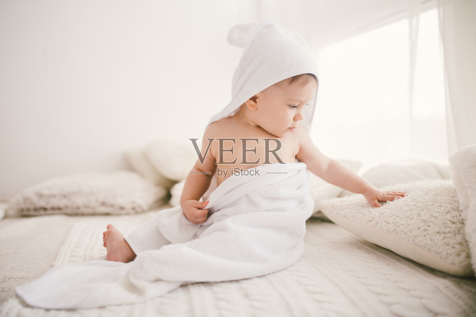 美丽微笑的新生男婴覆盖着白色的竹毛巾和有趣的耳朵。坐在一个白色针织，羊毛格子明亮的内部。从窗口向右照片摄影图片