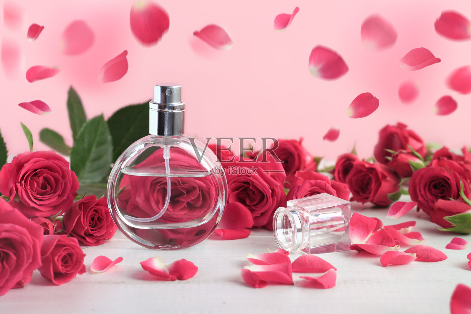 玫瑰香水瓶周围粉红色的新鲜玫瑰花蕾和飘落的花瓣。照片摄影图片