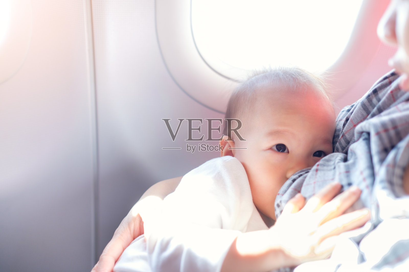 亚洲母亲正在母乳喂养可爱的小亚洲18个月的蹒跚学步的男婴在飞机上照片摄影图片