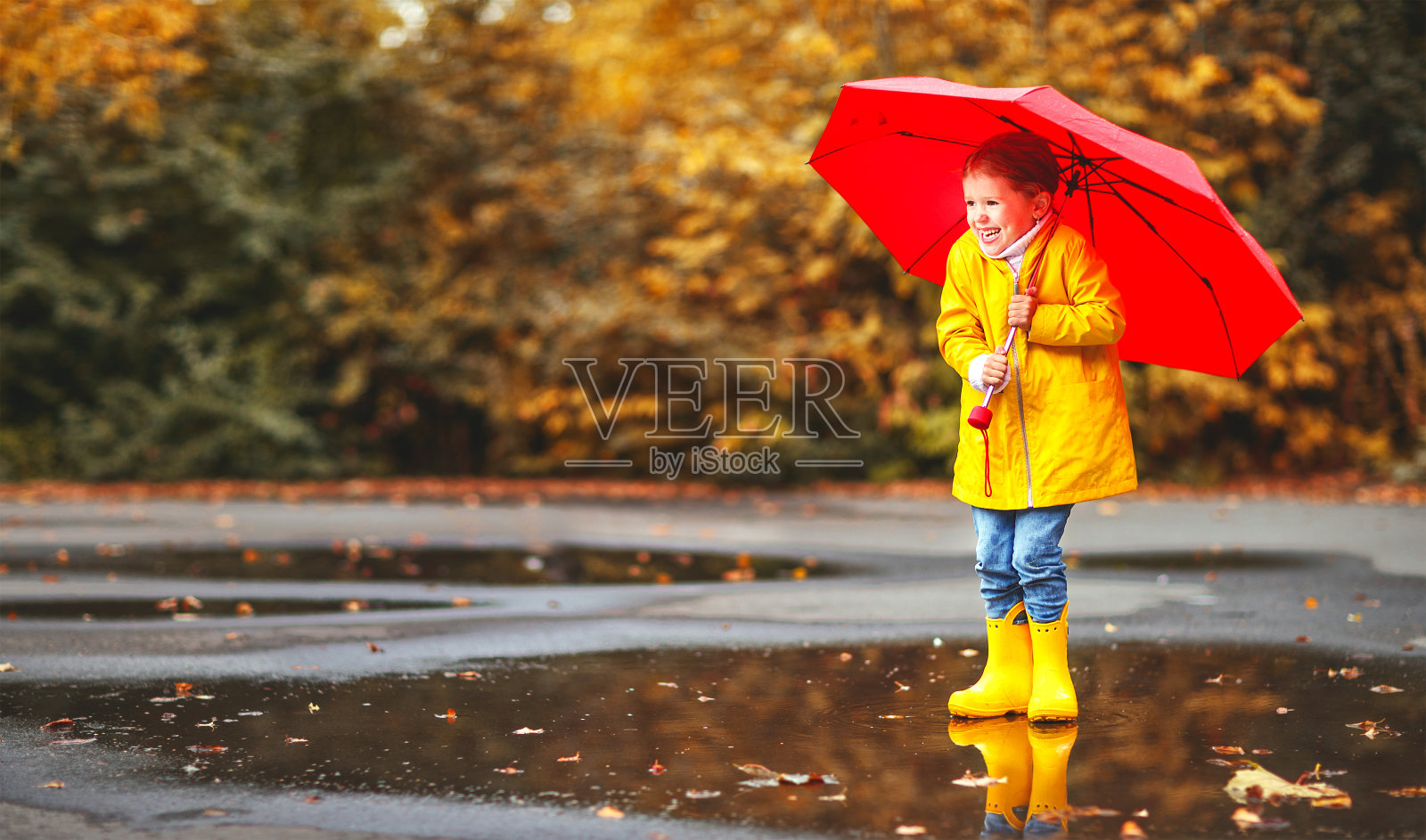 快乐的童女撑着伞，穿着胶靴在水坑里秋日漫步照片摄影图片