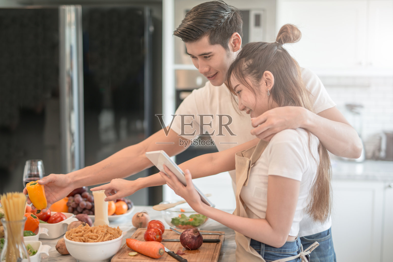 幸福的年轻夫妇在家里的厨房里一起做饭。看平板电脑照片摄影图片