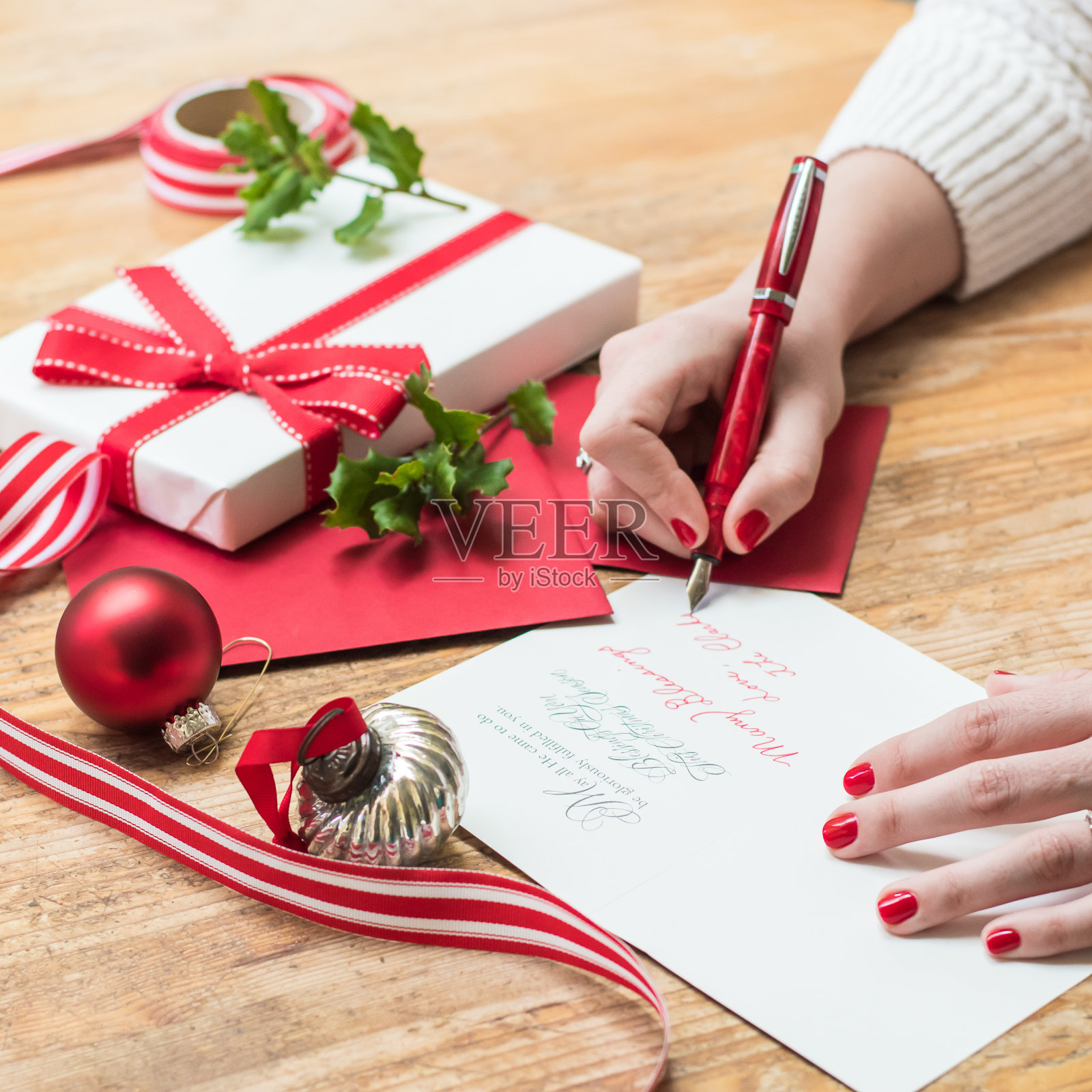 年轻女子用红指甲、红笔和节日装饰品写圣诞卡片照片摄影图片