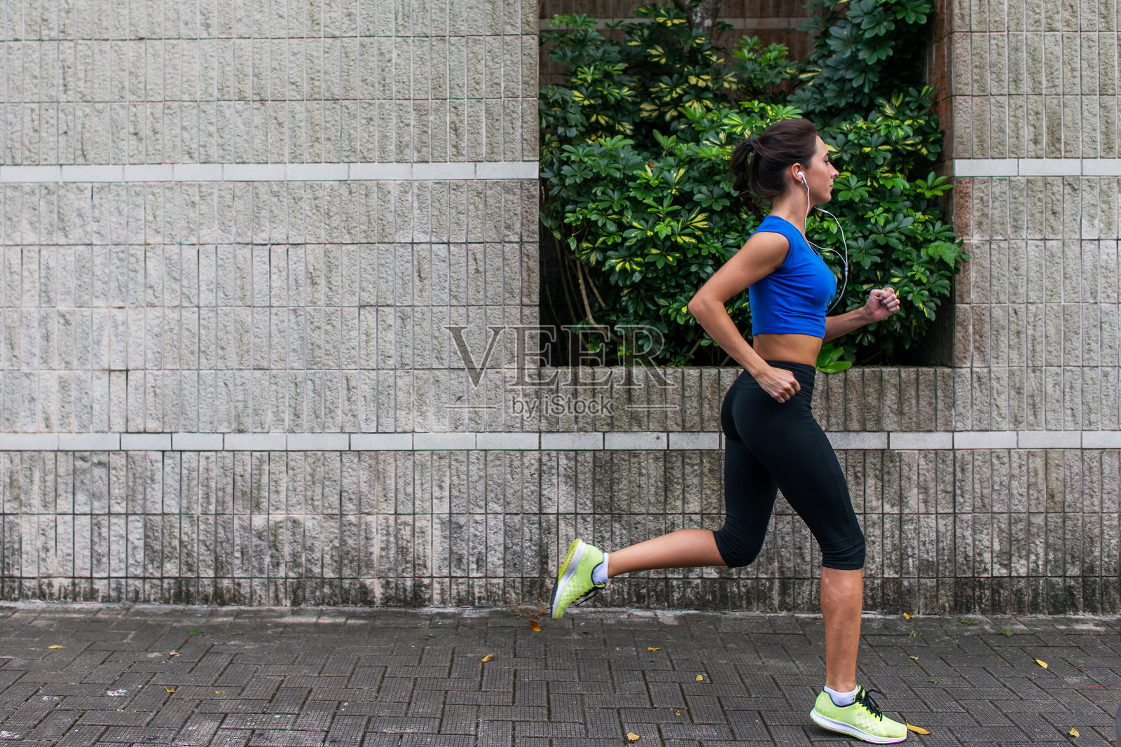 一个运动的年轻女人在户外工作的侧面视图。健身女孩在人行道上跑步。照片摄影图片