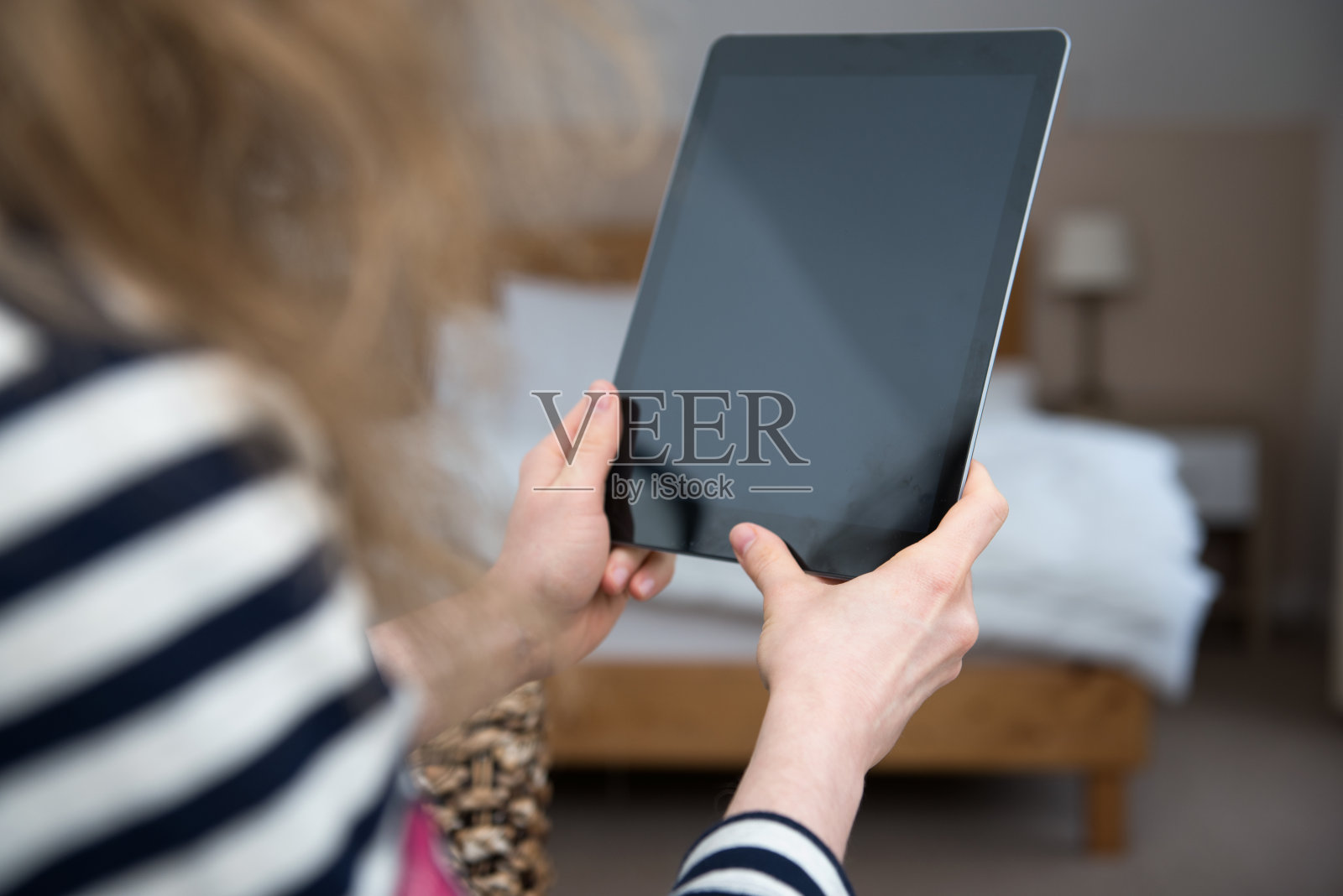 年轻的金发女人正坐在家里，手里拿着一台平板电脑。照片摄影图片