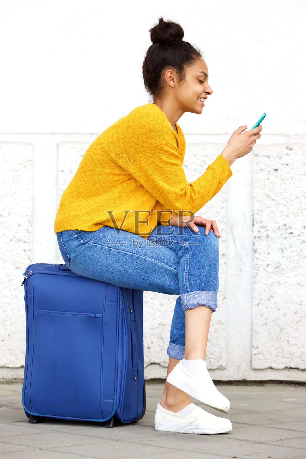 放松的女性旅行者坐在手提箱和使用手机照片摄影图片