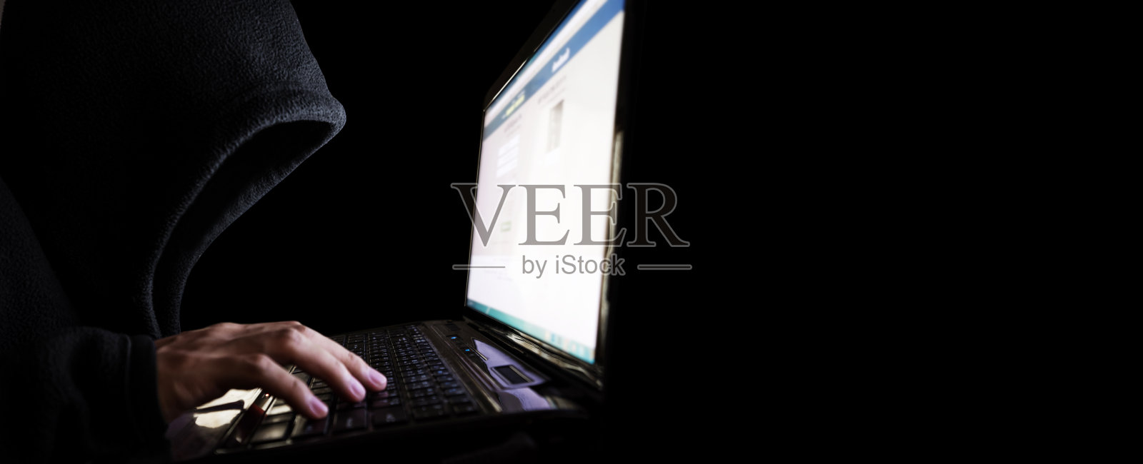 身份不明的黑兜帽黑客使用笔记本电脑。选择性聚焦，在全景黑色背景与复制空间照片摄影图片