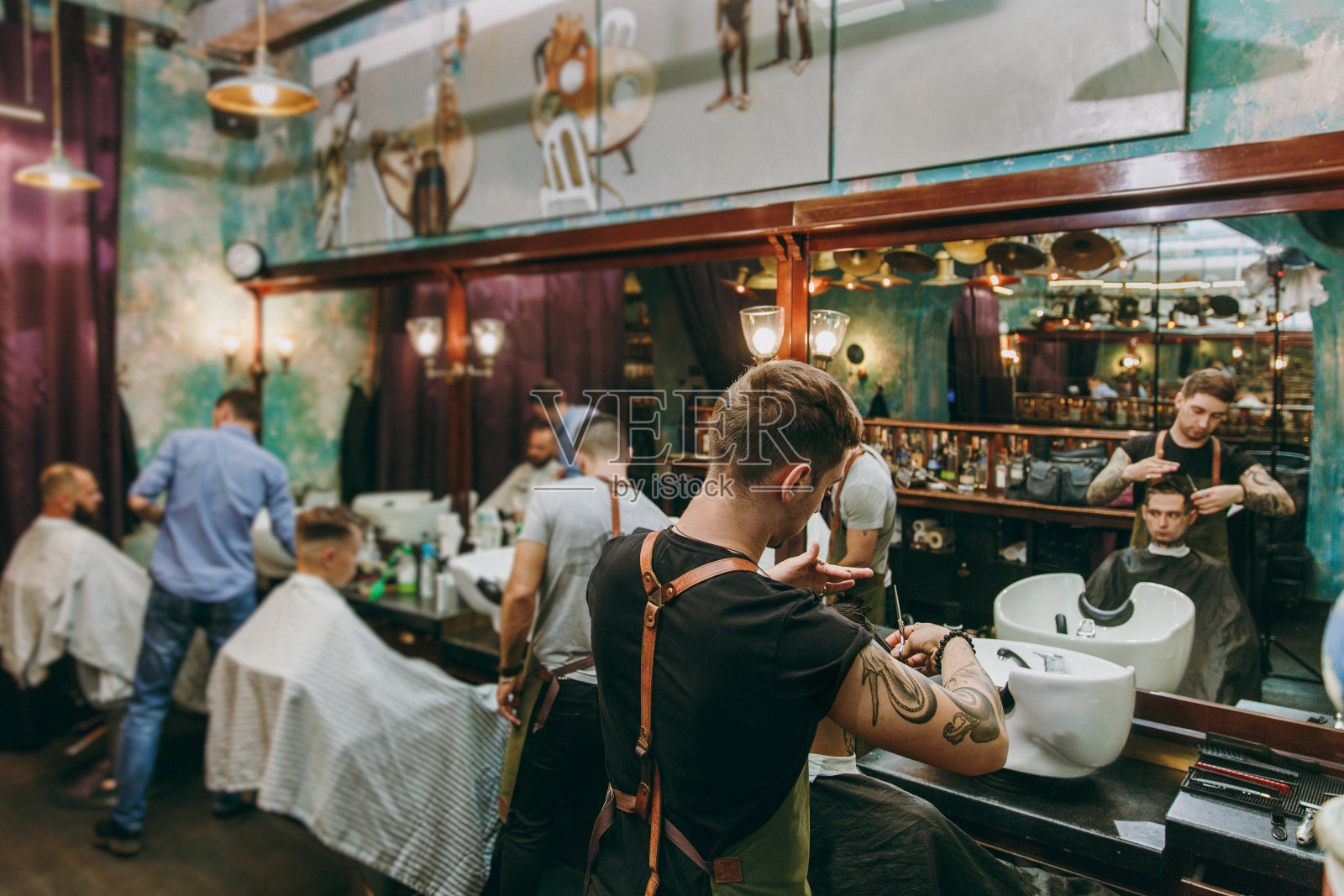 一个男人正在理发店里剪时髦的发型。男性发型师在纹身服务客户。照片摄影图片
