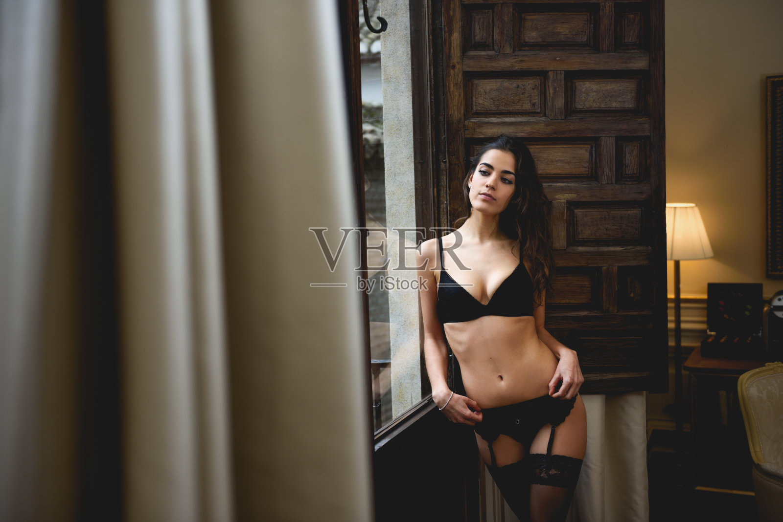 性感的年轻女人在内衣摆pose靠近一个窗口照片摄影图片