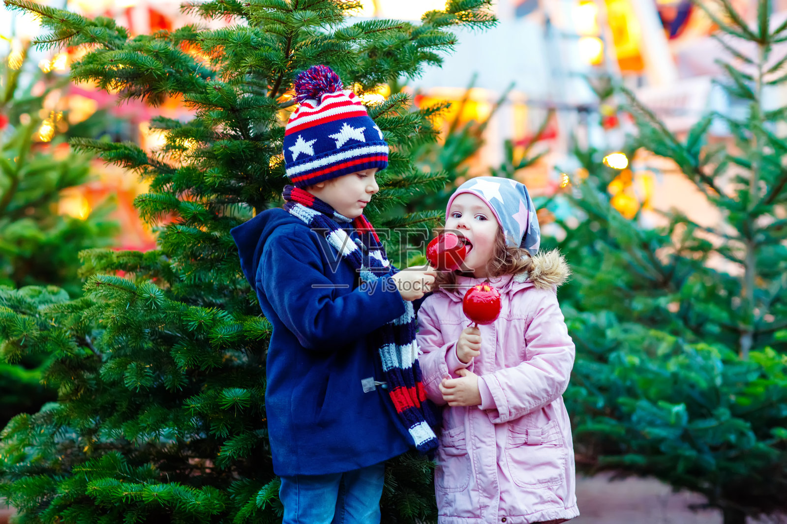 两个小孩在圣诞市场上吃糖苹果照片摄影图片