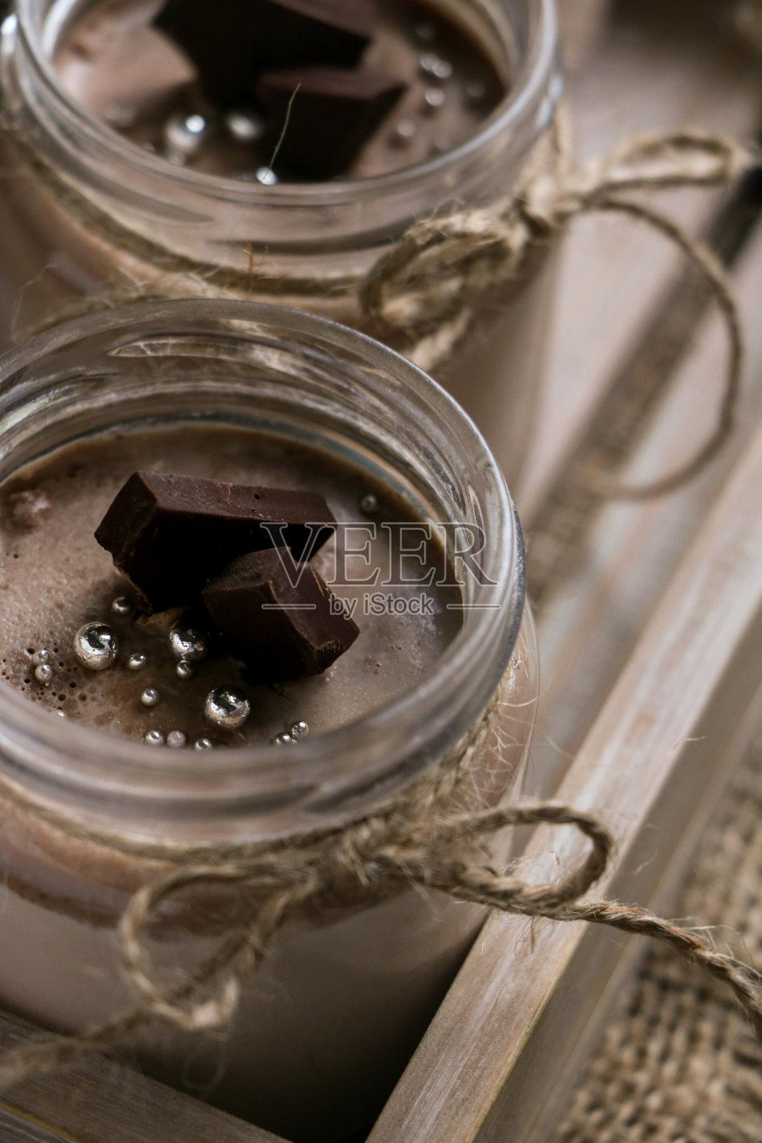 美味而甜蜜的甜点-巧克力意式奶冻放在两个玻璃罐里，用绳子绑着，黑色巧克力片，放在一个老式的木制托盘上照片摄影图片