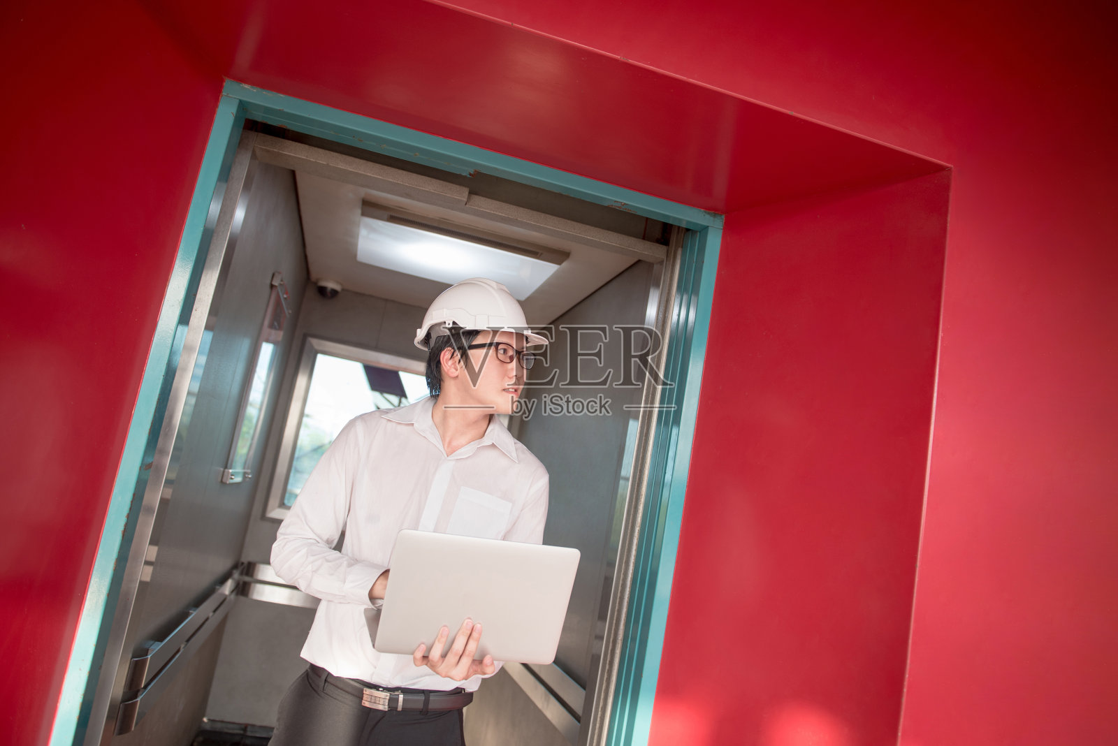 年轻的亚洲工程师或建筑师在被红墙包围的电梯里拿着笔记本电脑照片摄影图片