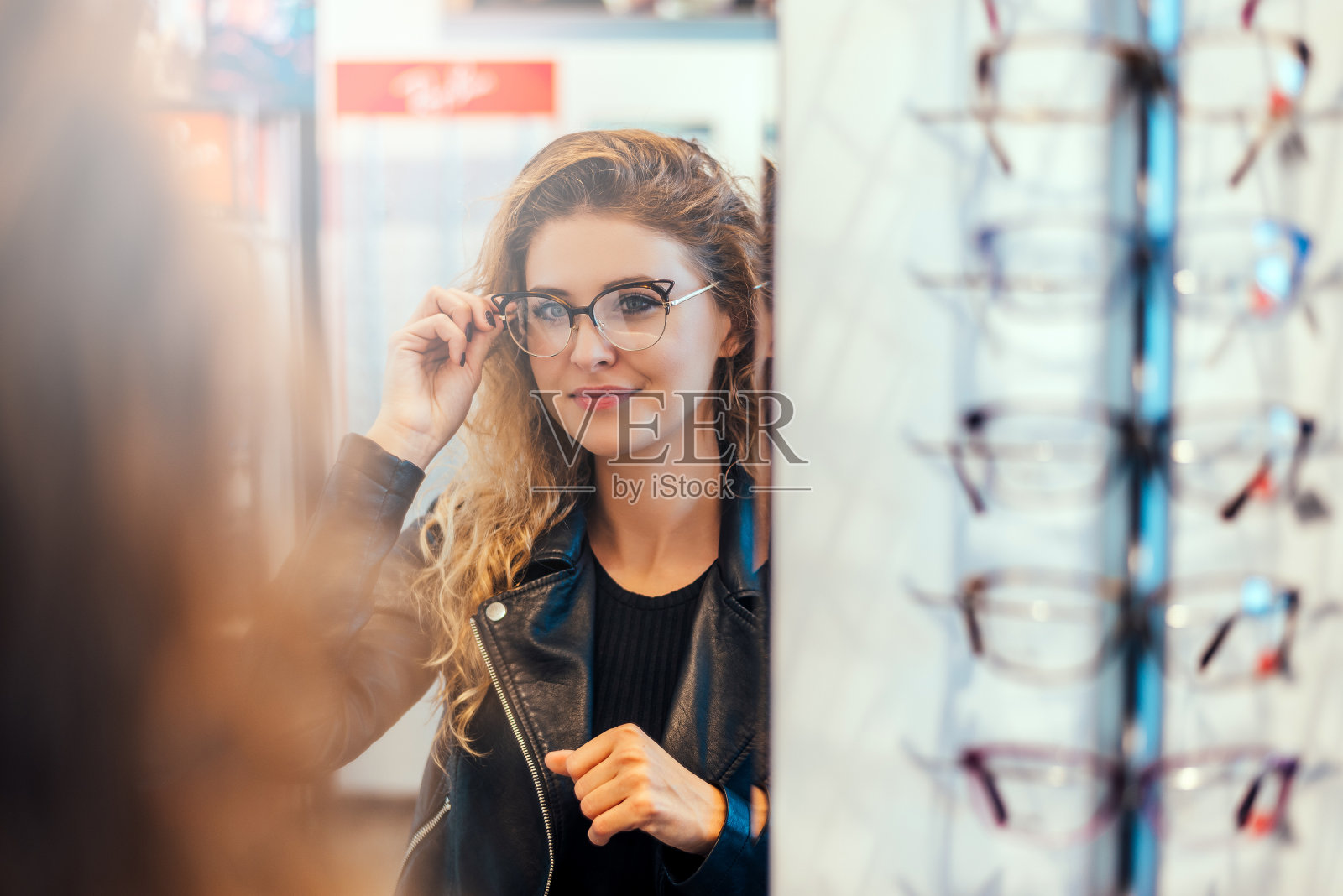 年轻女子微笑着在眼镜师的镜子上试眼镜。照片摄影图片